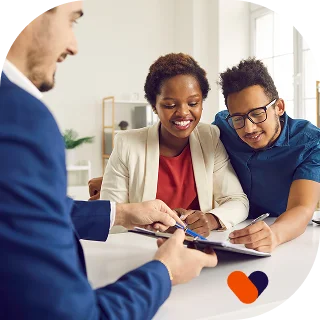 A smiling couple sits at a desk reviewing documents with an advisor in an office setting.