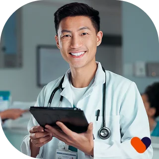 A smiling healthcare professional in blue scrubs holds a tablet in a modern medical setting.