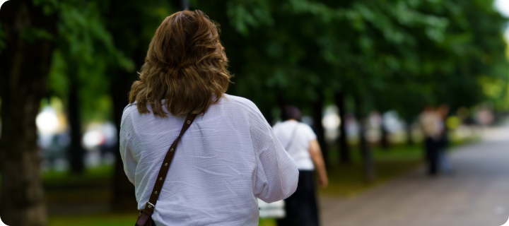 A group of individuals strolls along a wide pathway in a park surrounded by leafy trees, enjoying the pleasant weather in the late afternoon of a sunny day, walking to help manage afternoon slumps.