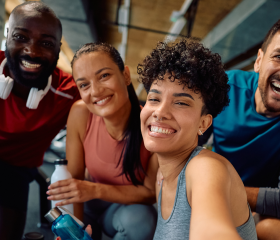 Multiracial group of happy athlete taking selfie in a gym and looking at camera. Focus is on African American woman.