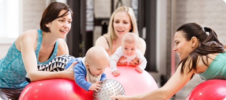 Baby movement class. Parents helping babies to improve motor skills, proper movement on fitball. Pediatric physical therapist leading class. Mothers exercising with babies.