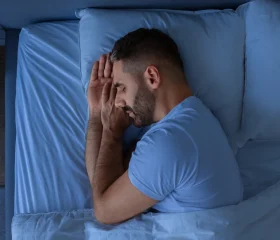 Guy Getting a Good Night’s Sleep, Holding Hands Near Face Enjoying Rest Lying In Cozy Bed In Modern Bedroom Interior. European Middle Aged Guy Healthy Sleep Concept.