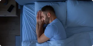Guy Getting a Good Night’s Sleep, Holding Hands Near Face Enjoying Rest Lying In Cozy Bed In Modern Bedroom Interior. European Middle Aged Guy Healthy Sleep Concept.
