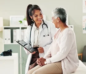 Doctor discussing health insurance options with an older patient during a medical office visit, representing HMO vs. PPO healthcare plans and choosing the right coverage.