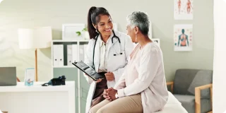 Doctor discussing health insurance options with an older patient during a medical office visit, representing HMO vs. PPO healthcare plans and choosing the right coverage.