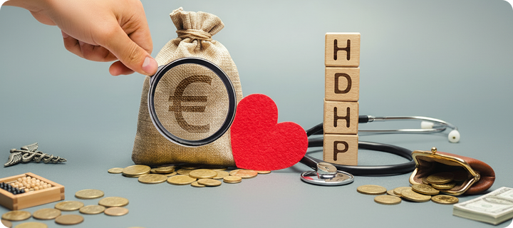 Wooden blocks spelling “HDHP” beside a red heart, stethoscope, coins, and money bag representing high-deductible health plan costs.
