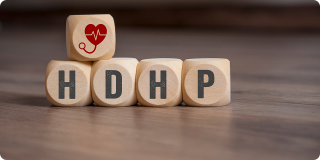 Wooden blocks spelling “HDHP” with a heart and stethoscope icon representing a high-deductible health plan.