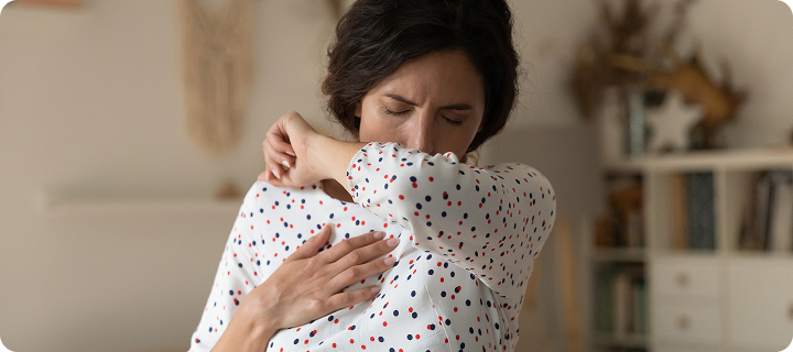 Woman coughing into her elbow at home, illustrating Coverage Fox guidance for cold and flu season.