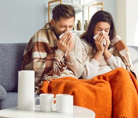 Sick couple resting at home with tissues and blankets, representing Coverage Fox guidance for cold and flu season.