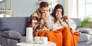 Sick couple resting at home with tissues and blankets, representing Coverage Fox guidance for cold and flu season.